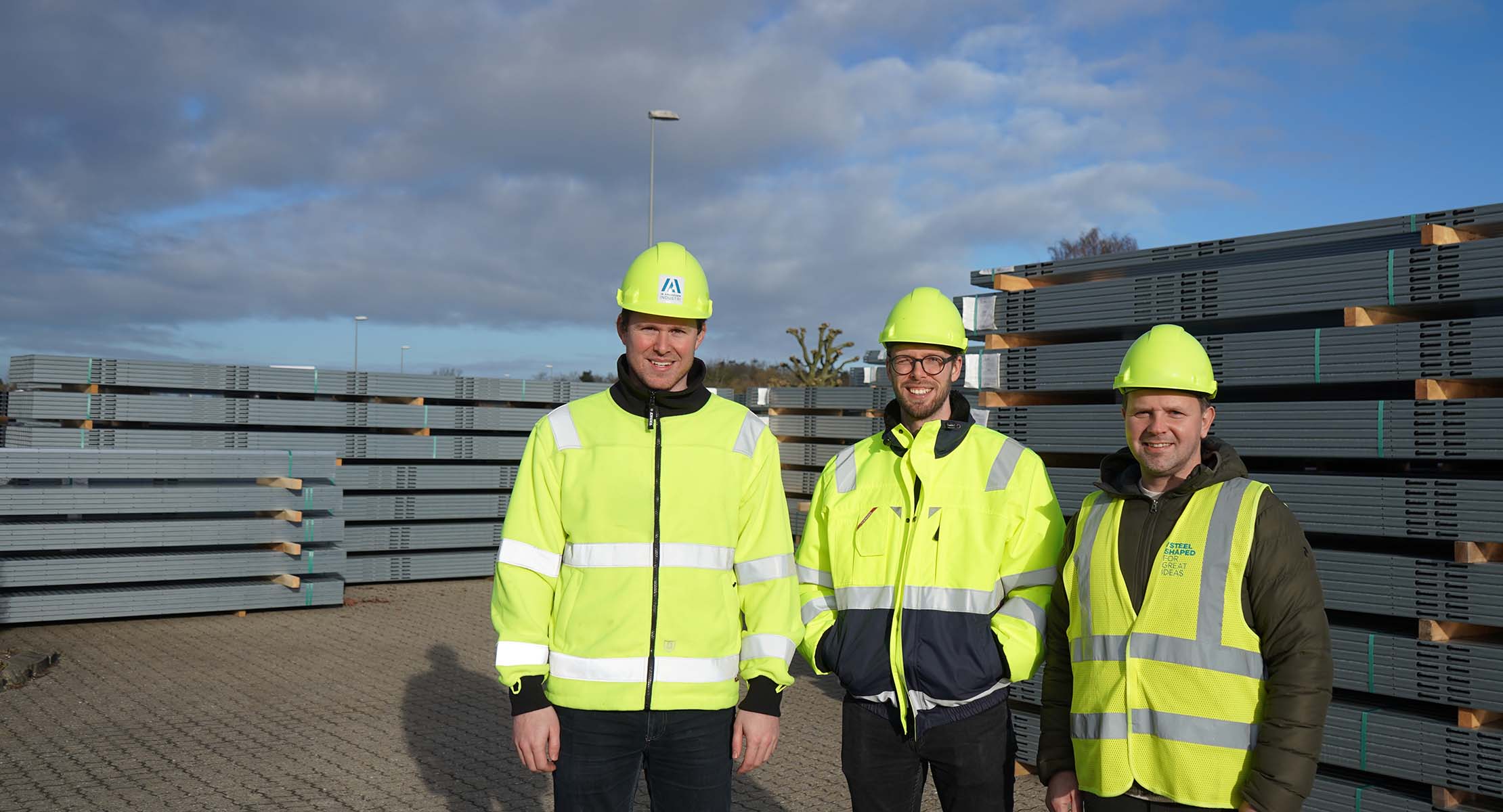 Tre medarbejdere poserer foran stålprofiler til solarprojekter
